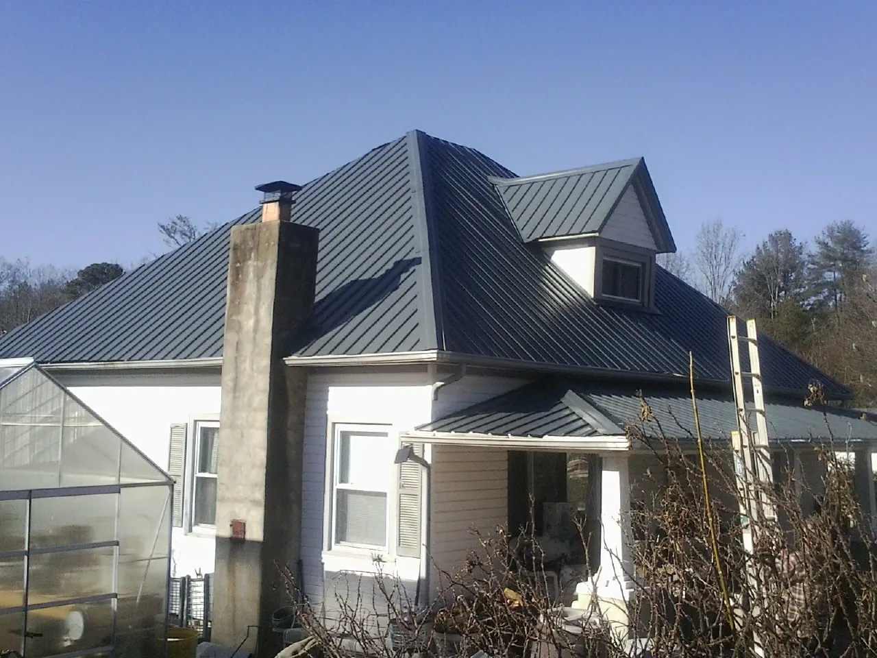 Dark blue standing seam metal roof on a white farmhouse with dormer — Slate & Tile Roof Repair by Roofing Brothers in Moreland