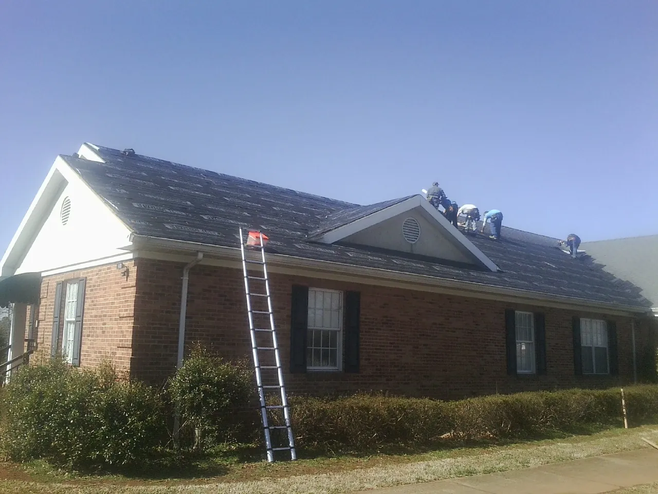 Crew tearing shingles off a brick ranch roof with a ladder set — Metal Roof Repair work by our crew in Moreland