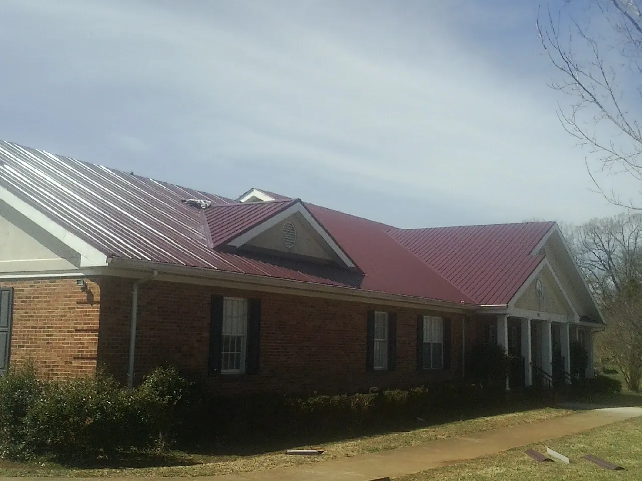 Red metal roof with gabled entries on a long brick building, from a Hail Damage Roof Repair job in Moreland