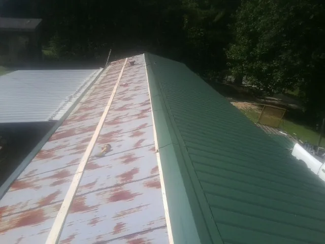 Old rusted panels beside newly installed green metal roofing — Wind Damage Roof Repair by Roofing Brothers in Moreland