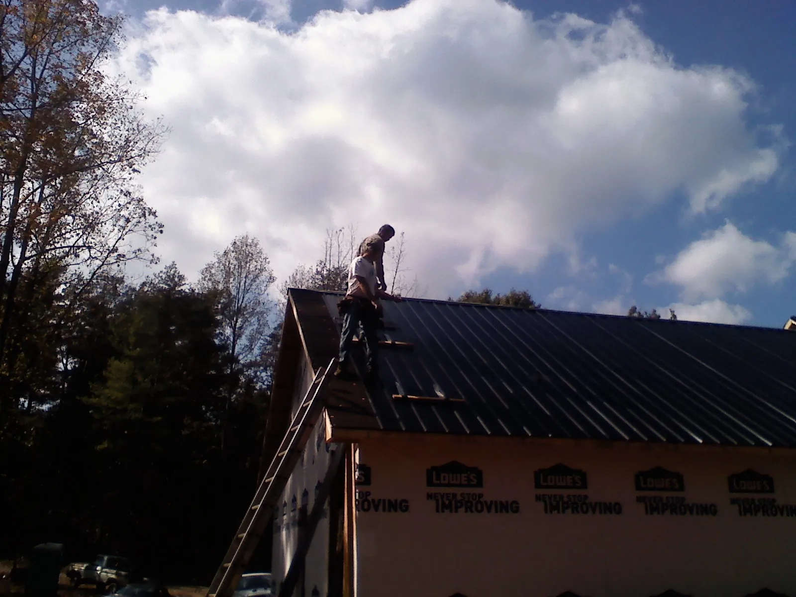Roofer fastening dark metal panels high against a cloudy sky, from a Roof Inspection job in Moreland
