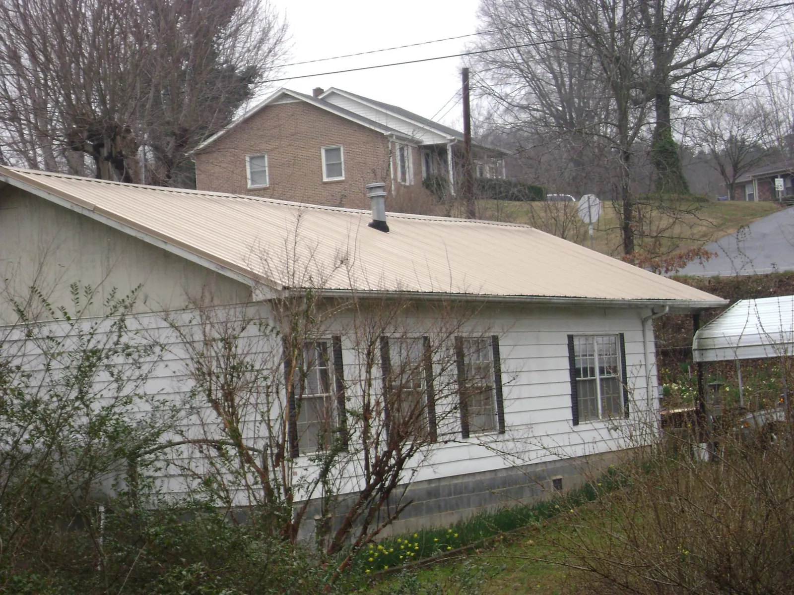 Tan metal roof on a white sided house set into a hillside — Commercial Roofing by Roofing Brothers in Moreland