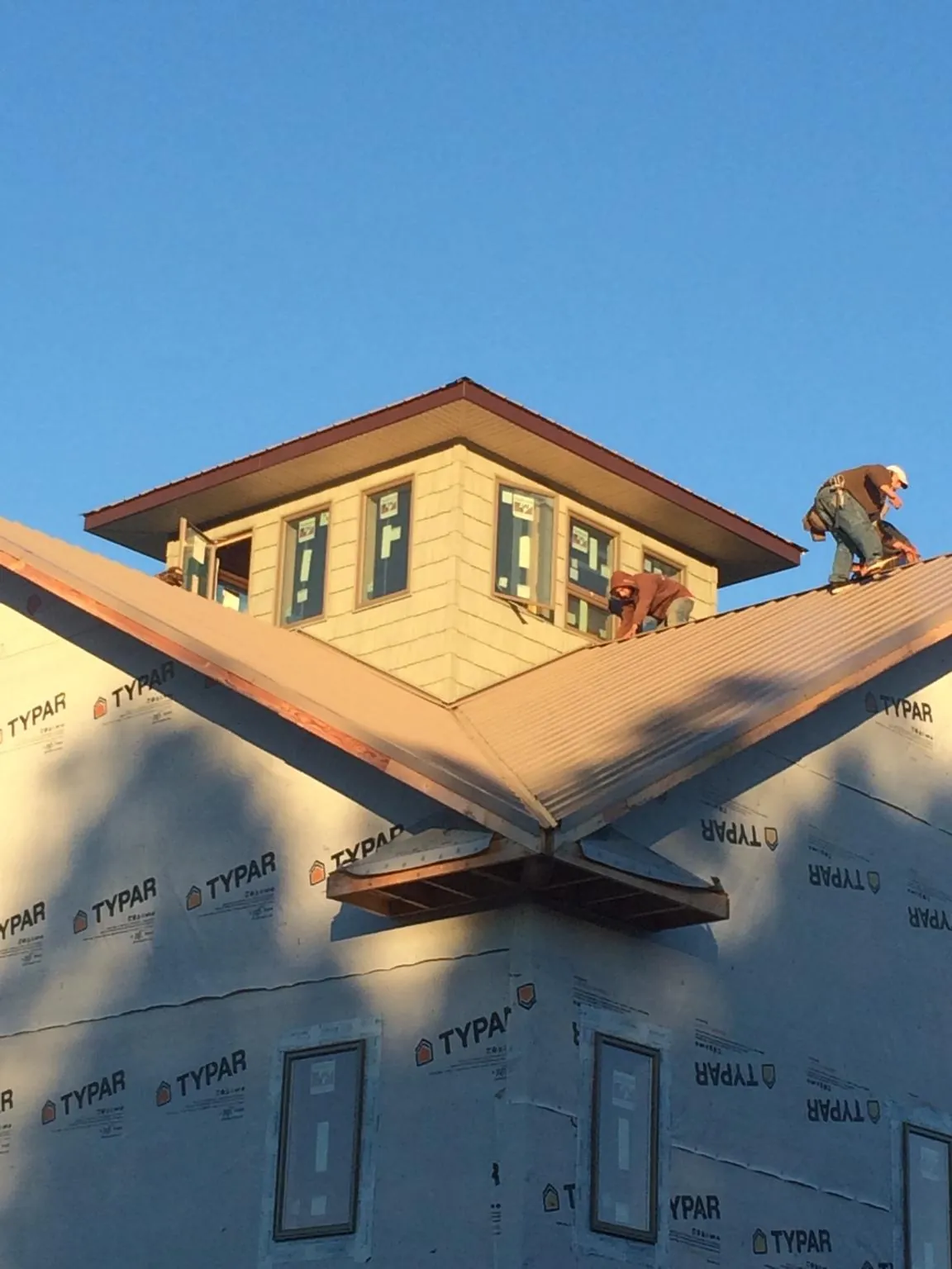 Roofers working around a rooftop cupola on a new metal roof at sunset in Moreland